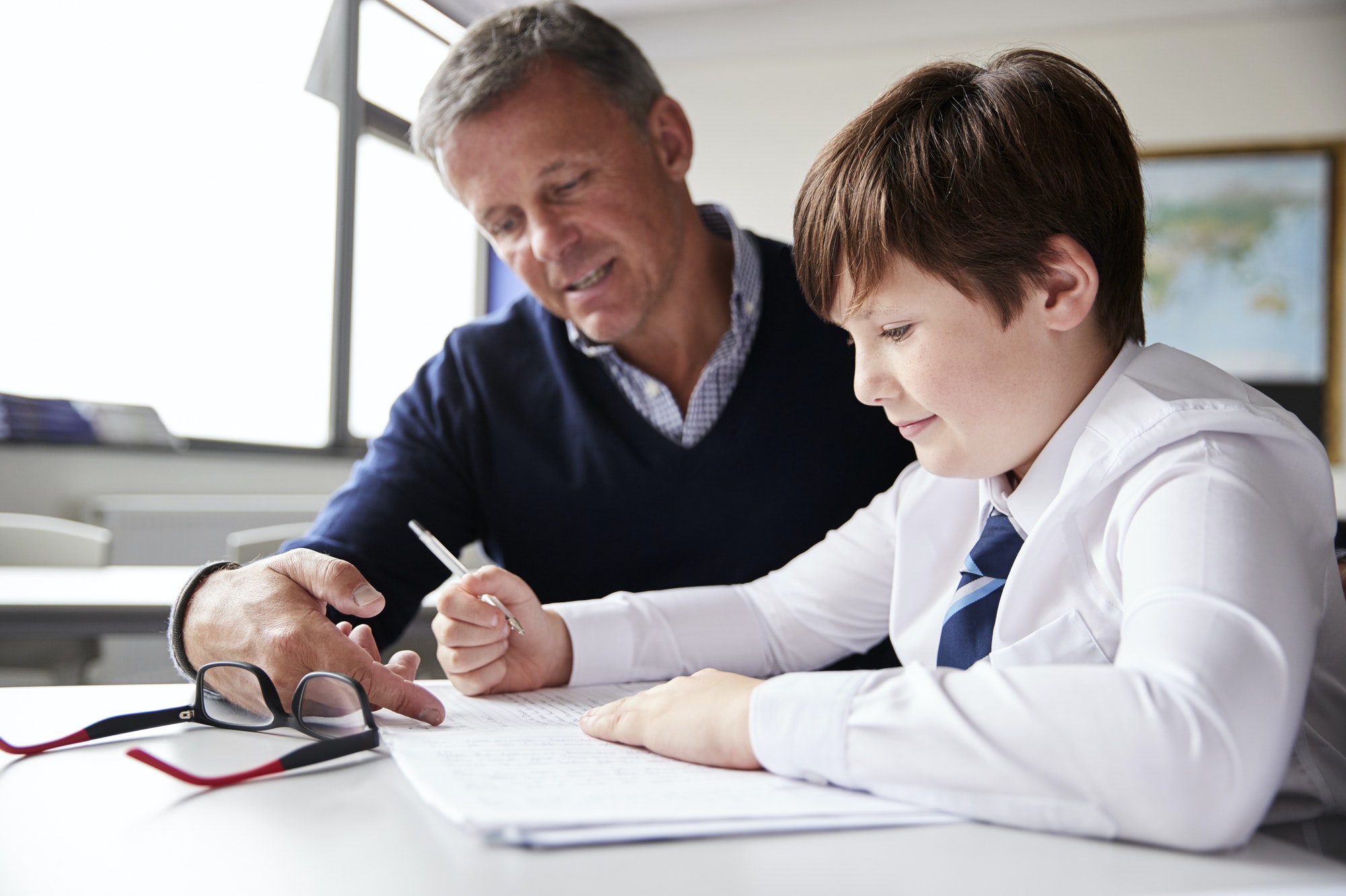 High School Tutor Giving Male Student Wearing Uniform One To One Tuition At Desk
